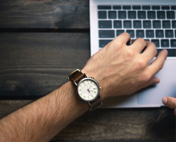 Hand mit Armbanduhr im Hintergrund die Tastatur eines Laptops